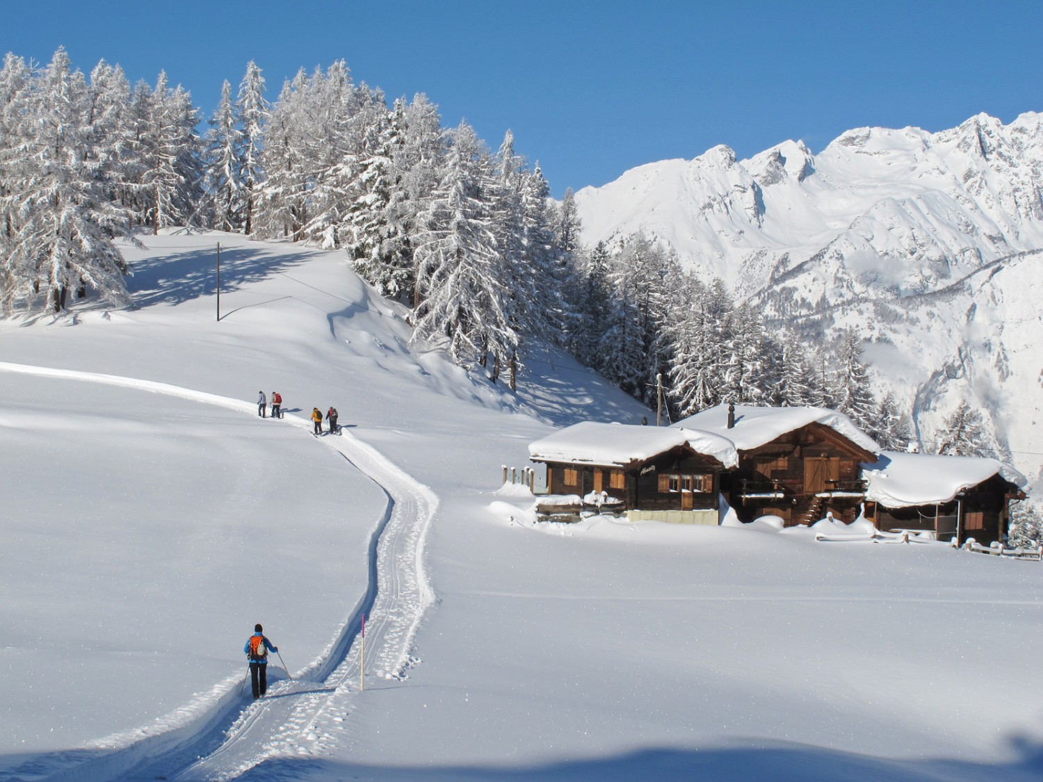 Au bord d’un vaste plateau très enneigé se dressent de petites cabanes en bois. Photo: Bürchen Unterbäch Tourismus