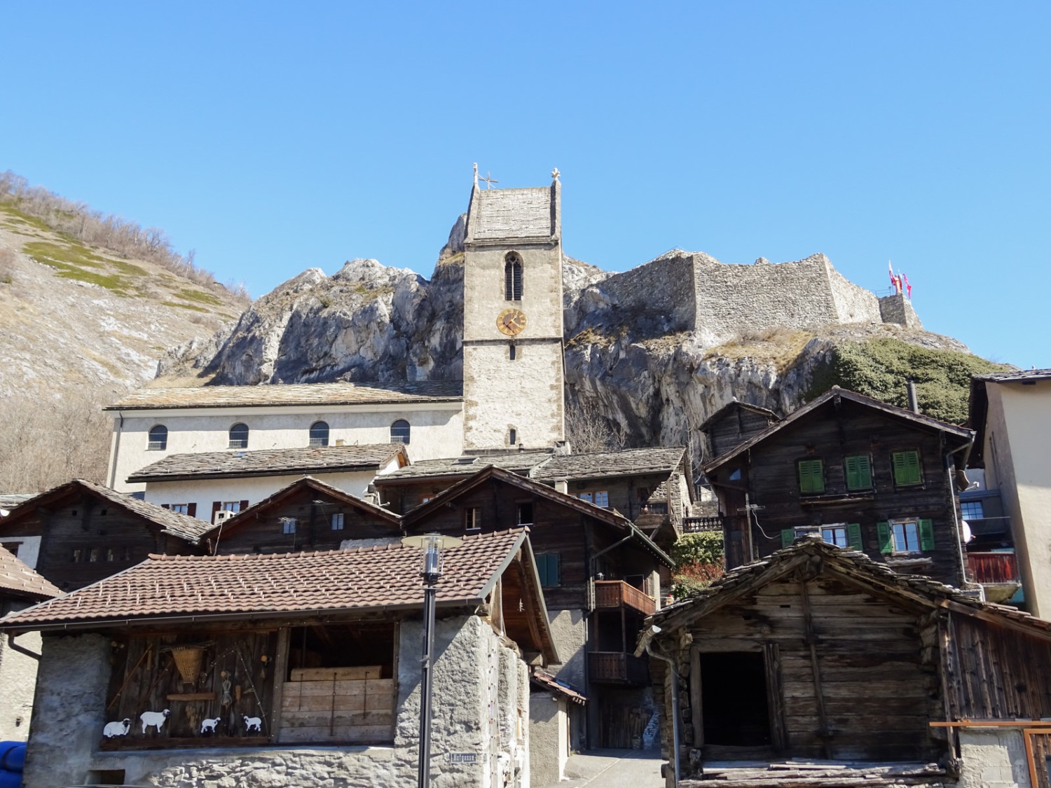 Hinter der Kirche von Niedergesteln flattern die Fahnen der Burg im Wind. Foto: Sabine Joss